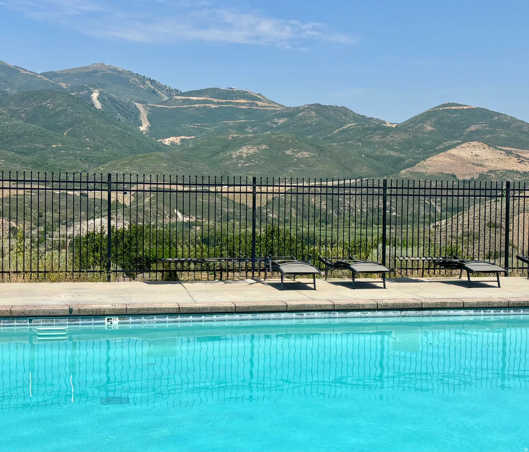 Swimming pool with concrete decking and a black metal fence, overlooking expansive mountains with visible ski runs