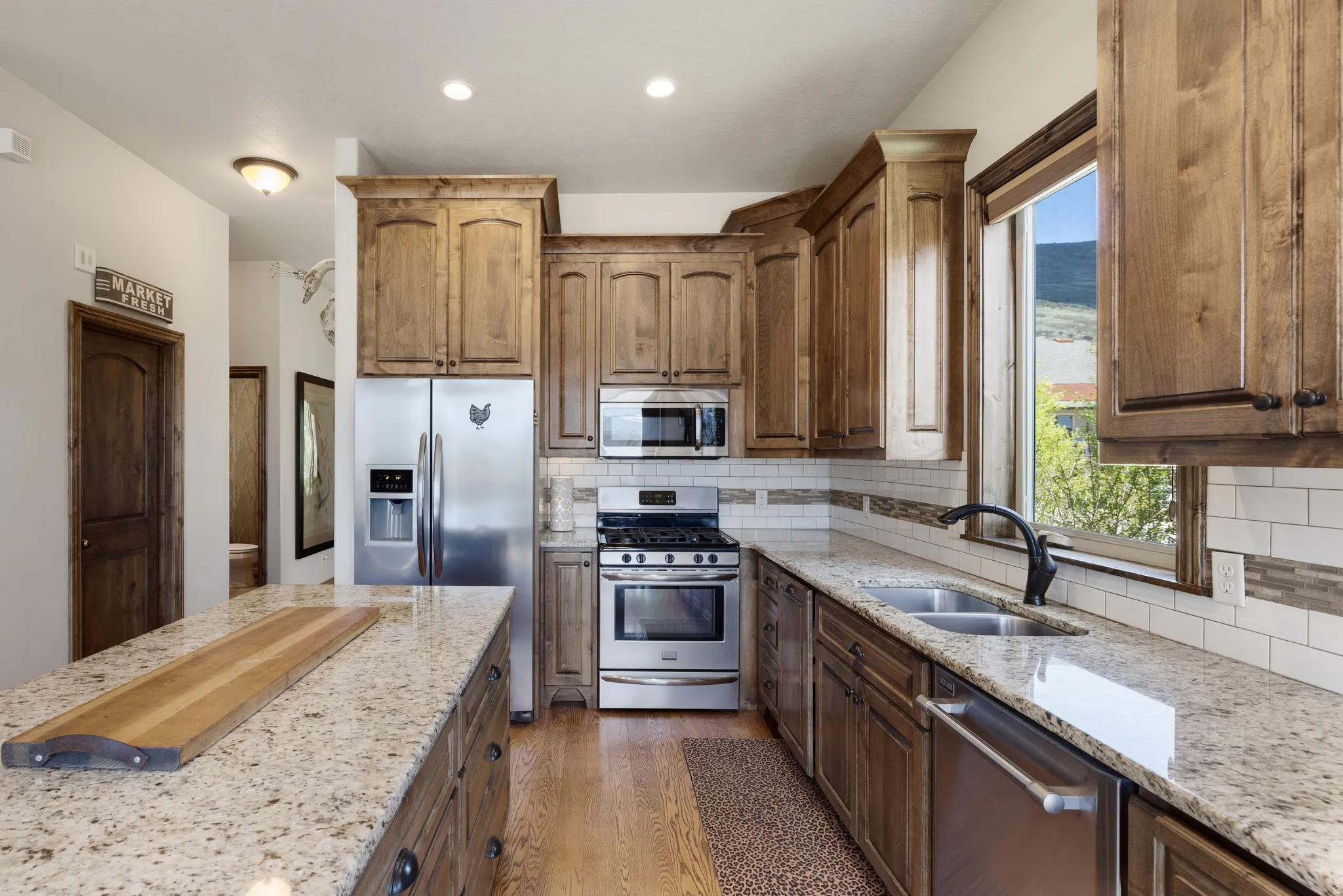 Kitchen featuring wood-finish cabinetry, stainless steel appliances, speckled stone countertops, and a subway tile backsplash
