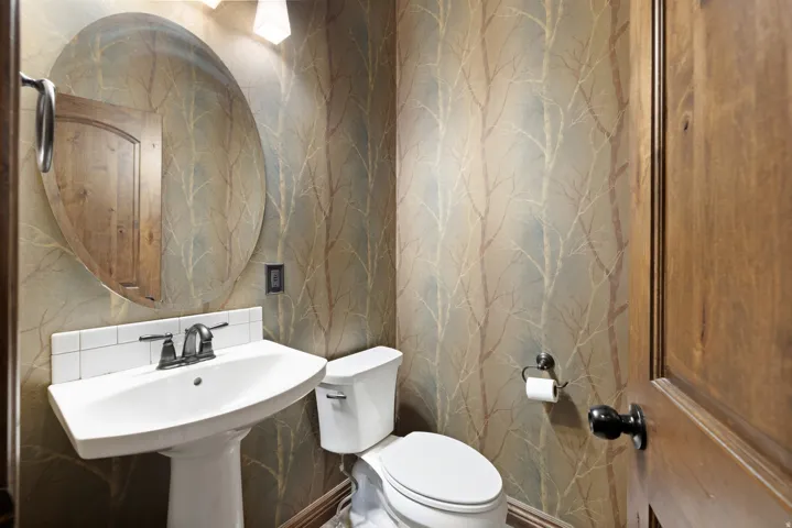 Pedestal sink with an oval mirror, accented by a subtle patterned wallpaper