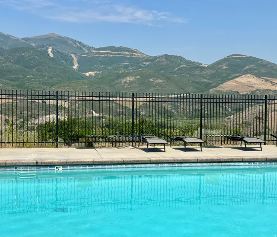 Swimming pool with concrete decking and a black metal fence, overlooking expansive mountains with visible ski runs