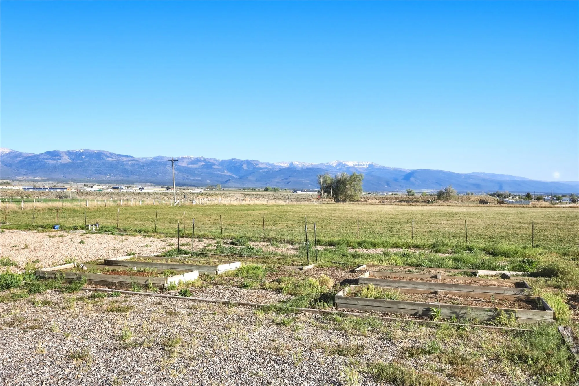 Expansive open land featuring two raised garden beds, a gravel-covered area, and a distant mountain range backdrop