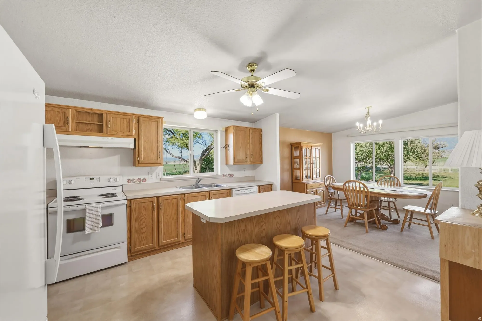Kitchen and dining area featuring wood-finish cabinetry, white appliances, and a central island with countertop seating