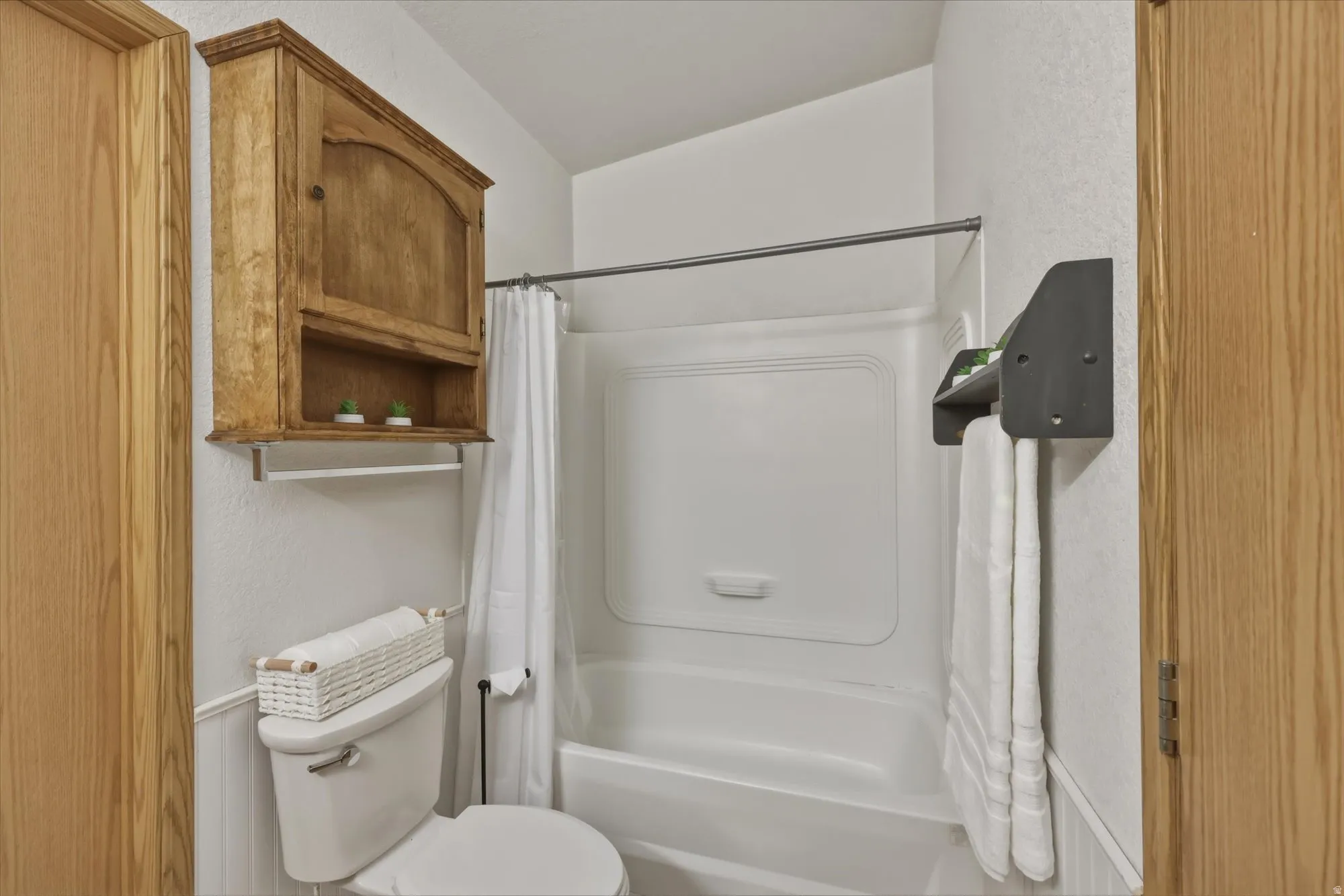 Bathroom featuring a white tub/shower combination, white toilet, wainscoting, and wood-finish cabinetry