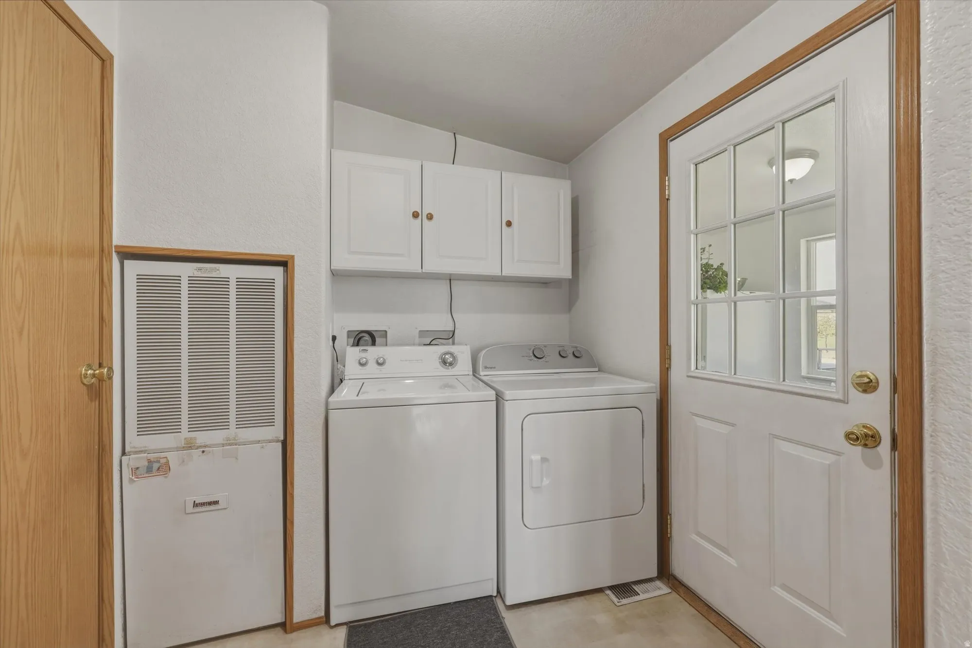 Dedicated utility area featuring white cabinetry with brass hardware, a white paneled door with divided lite glass, and light wood-finish trim