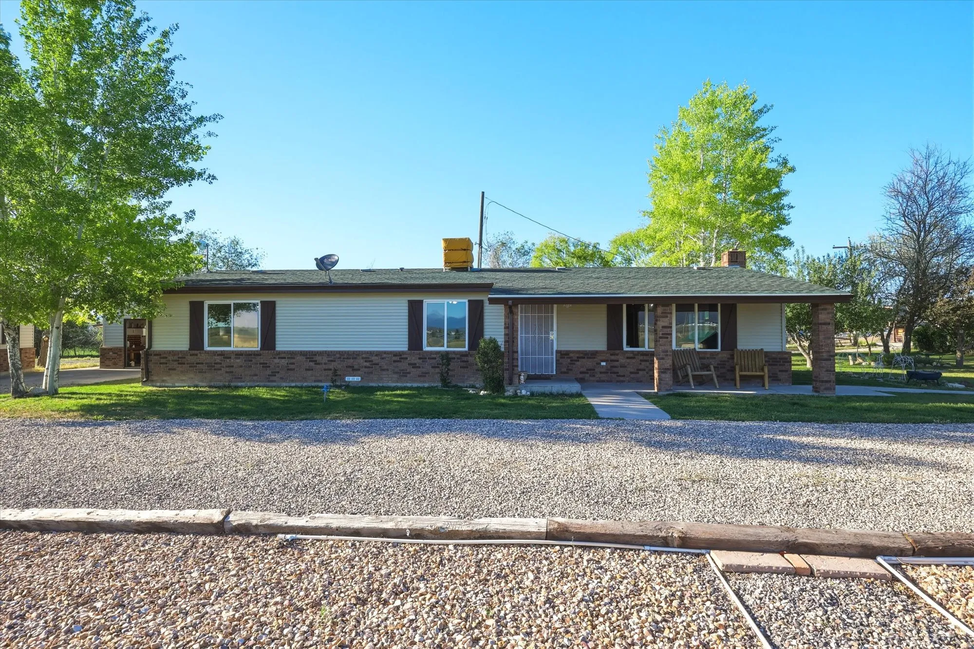 Ranch-style residence featuring a gravel driveway, mature trees, and a covered front porch with brick columns