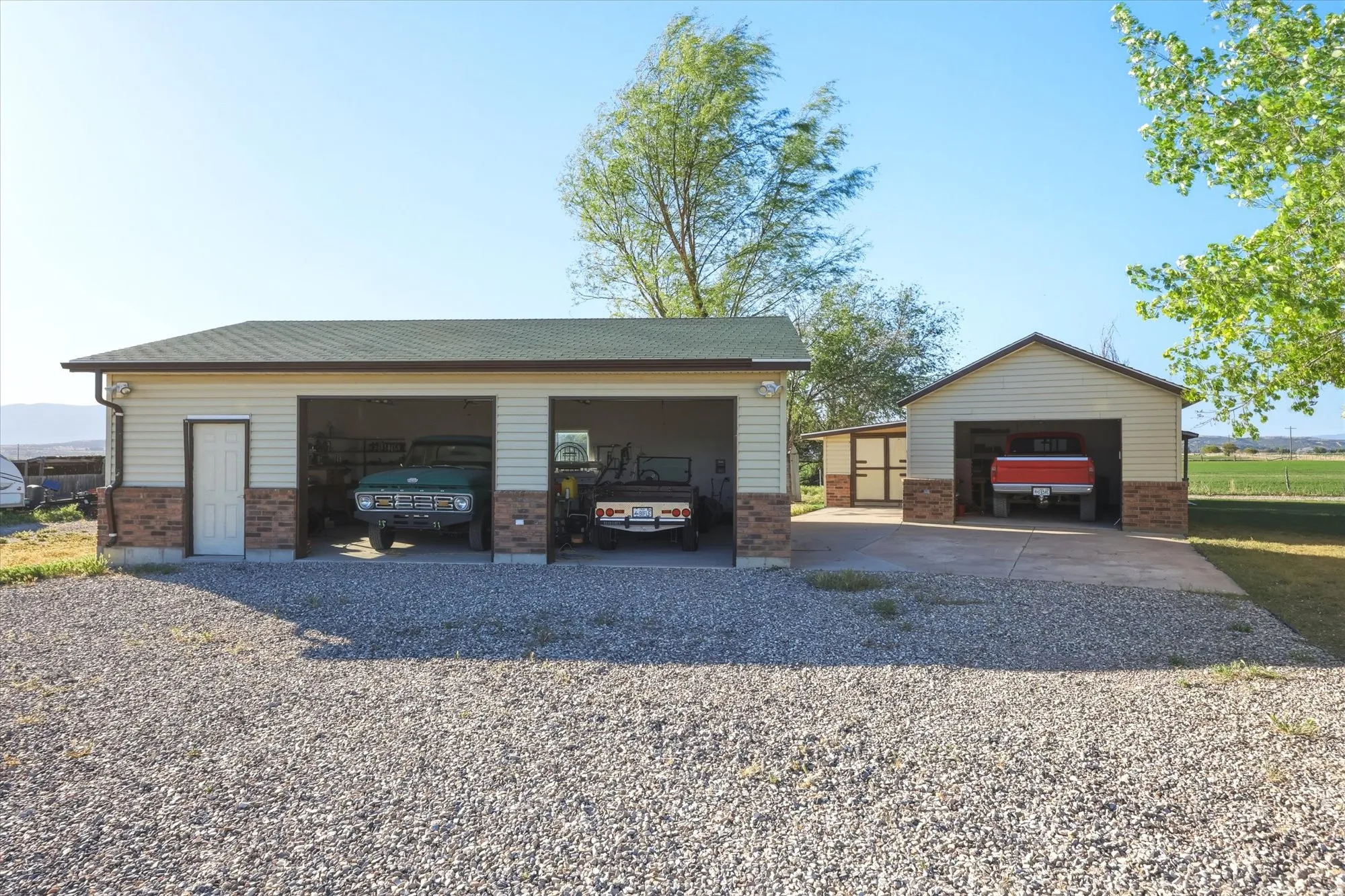 Two detached garages with light beige siding and a dark brown brick-finish wainscoting