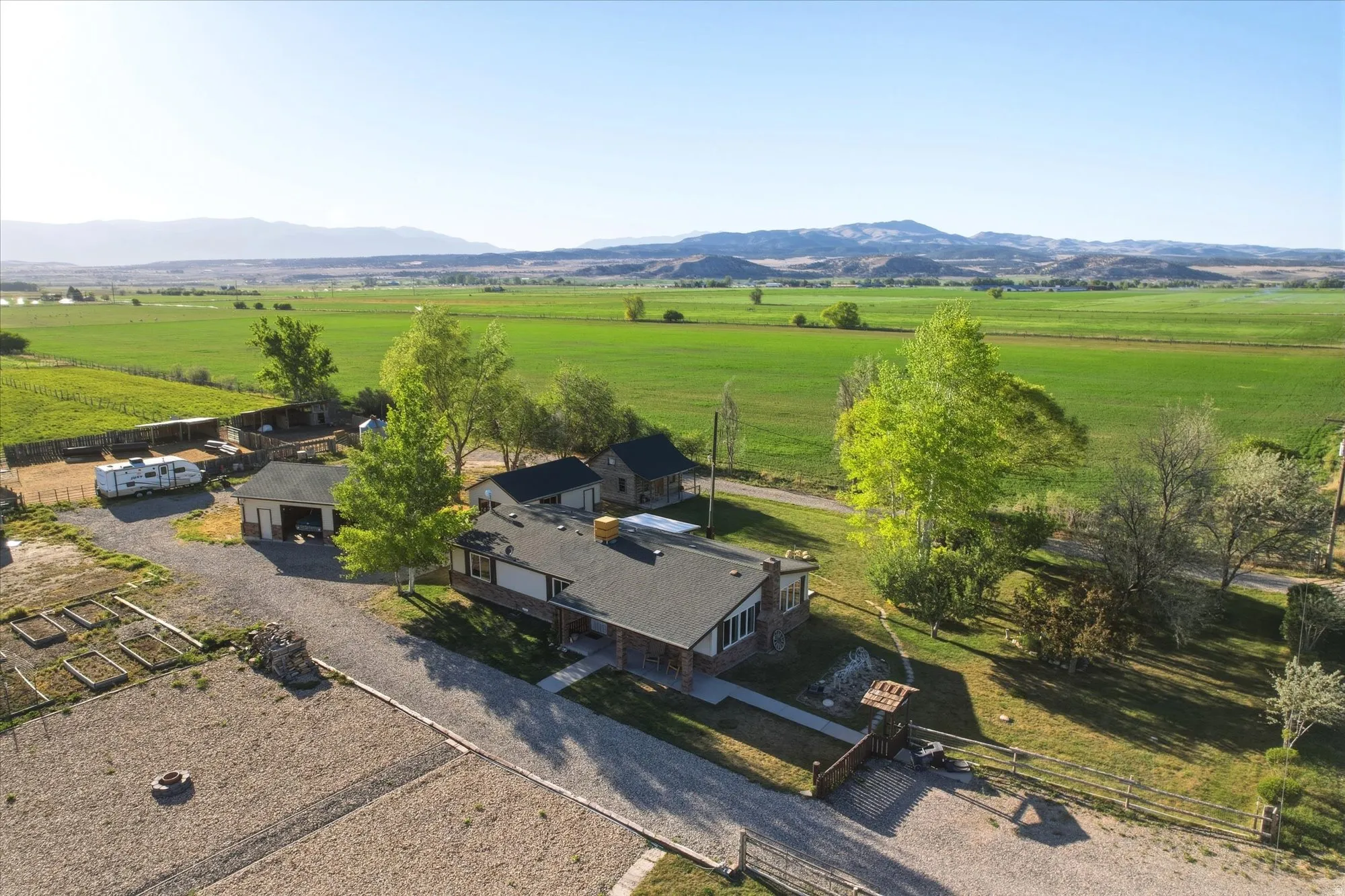 Spacious property featuring a main residence with a dark shingle roof, multiple outbuildings, and a gravel driveway