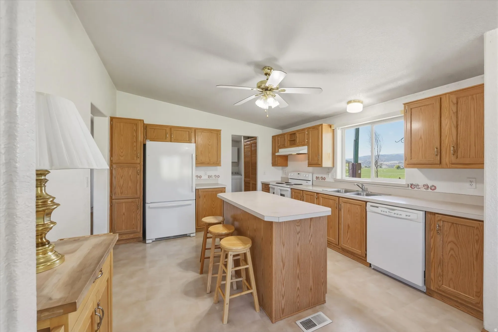 Kitchen featuring wood-finish cabinetry, white appliances, and a central island with countertop space