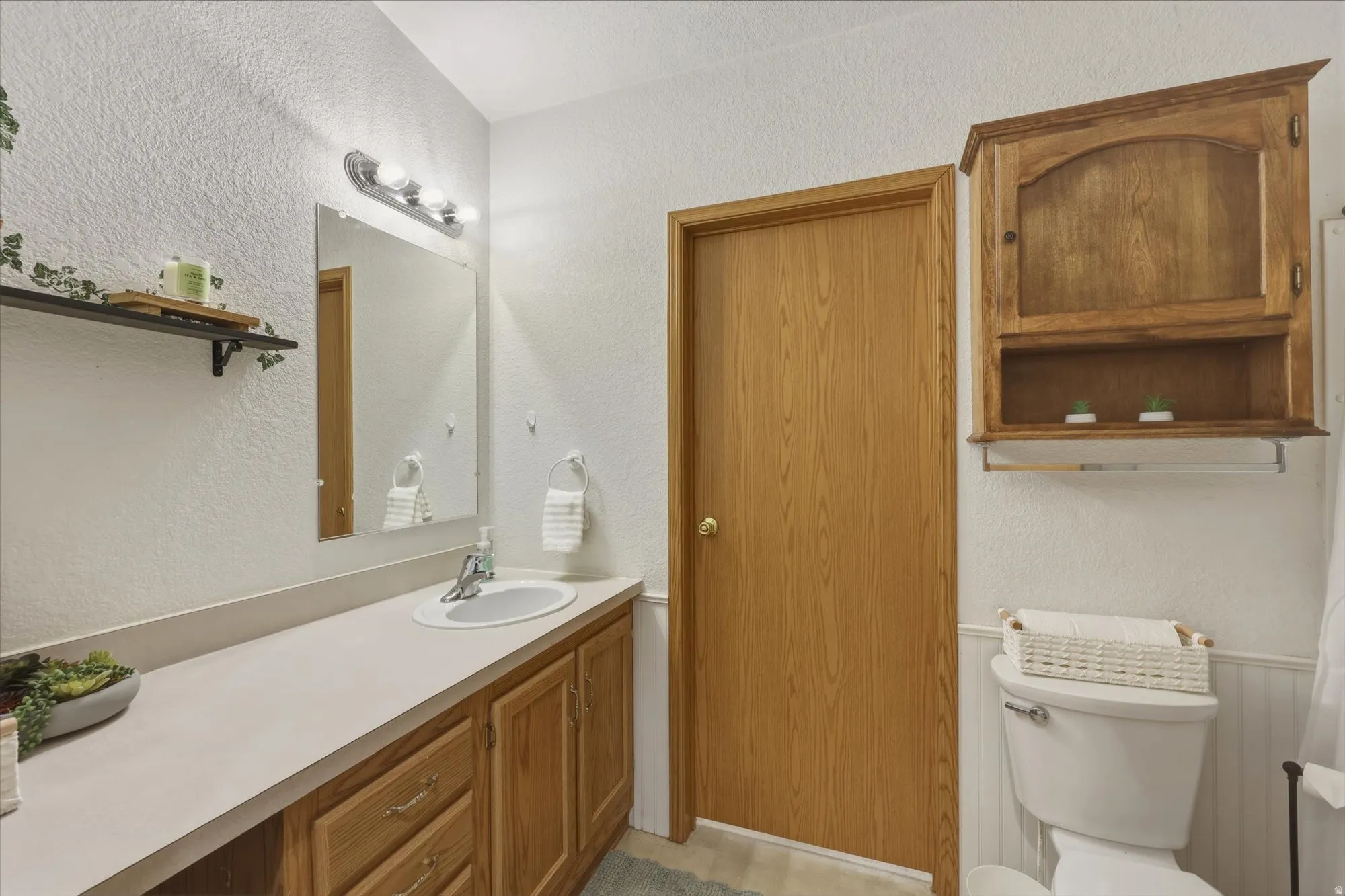 Bathroom featuring a light wood-finish vanity with an integrated sink, a wall-mounted mirror, and a three-light fixture