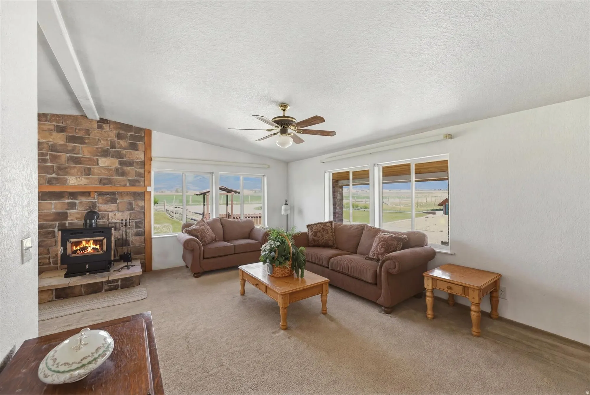 Spacious living area featuring a brick accent wall with a wood-burning stove, vaulted ceilings, and a ceiling fan