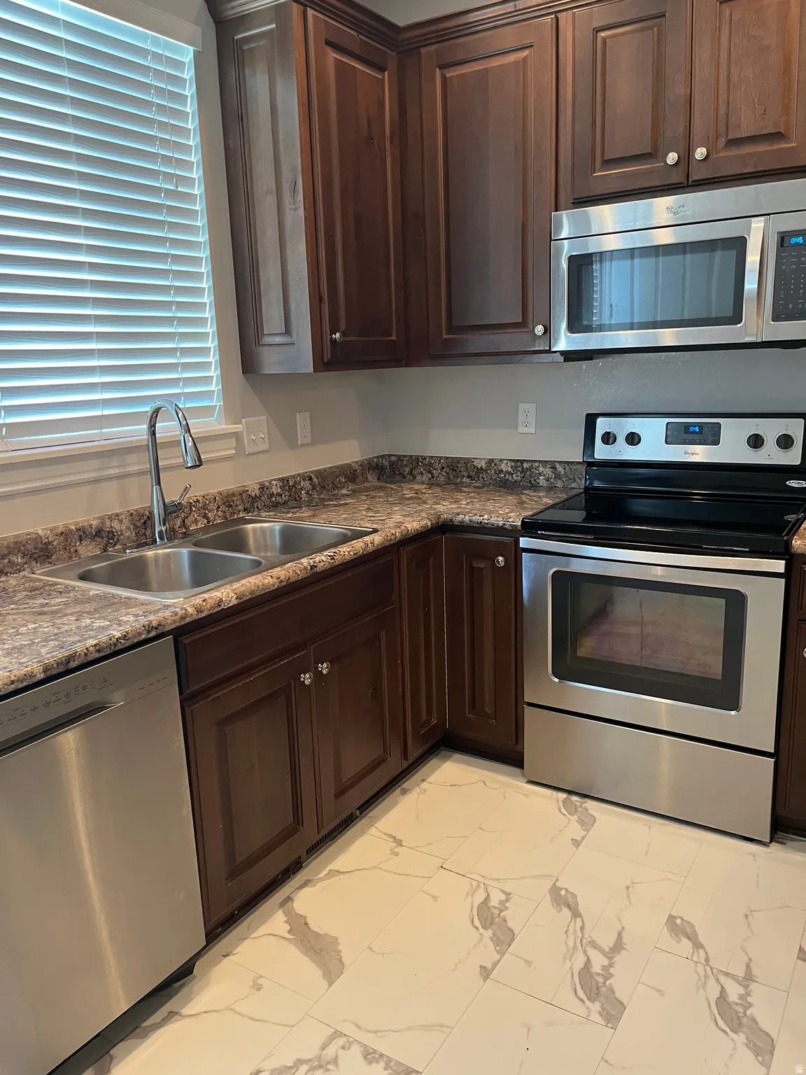 Kitchen featuring dark wood cabinetry, stainless steel appliances, a double basin sink, and patterned flooring