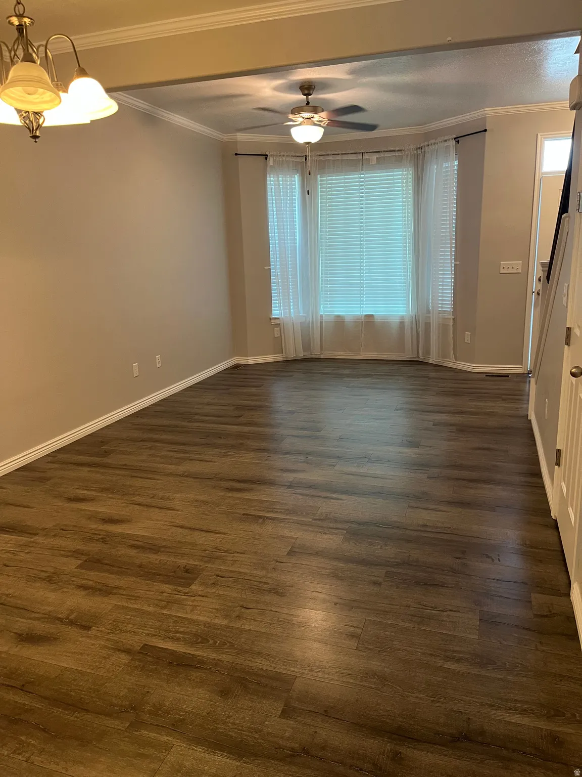 Spacious room featuring wood-finish flooring, a bay window with blinds and sheer curtains, a ceiling fan, and crown molding