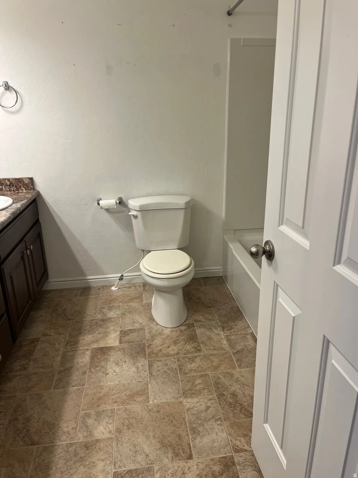 Bathroom featuring a white toilet, tile-patterned flooring, a dark wood-finish vanity with a countertop, and a white paneled door