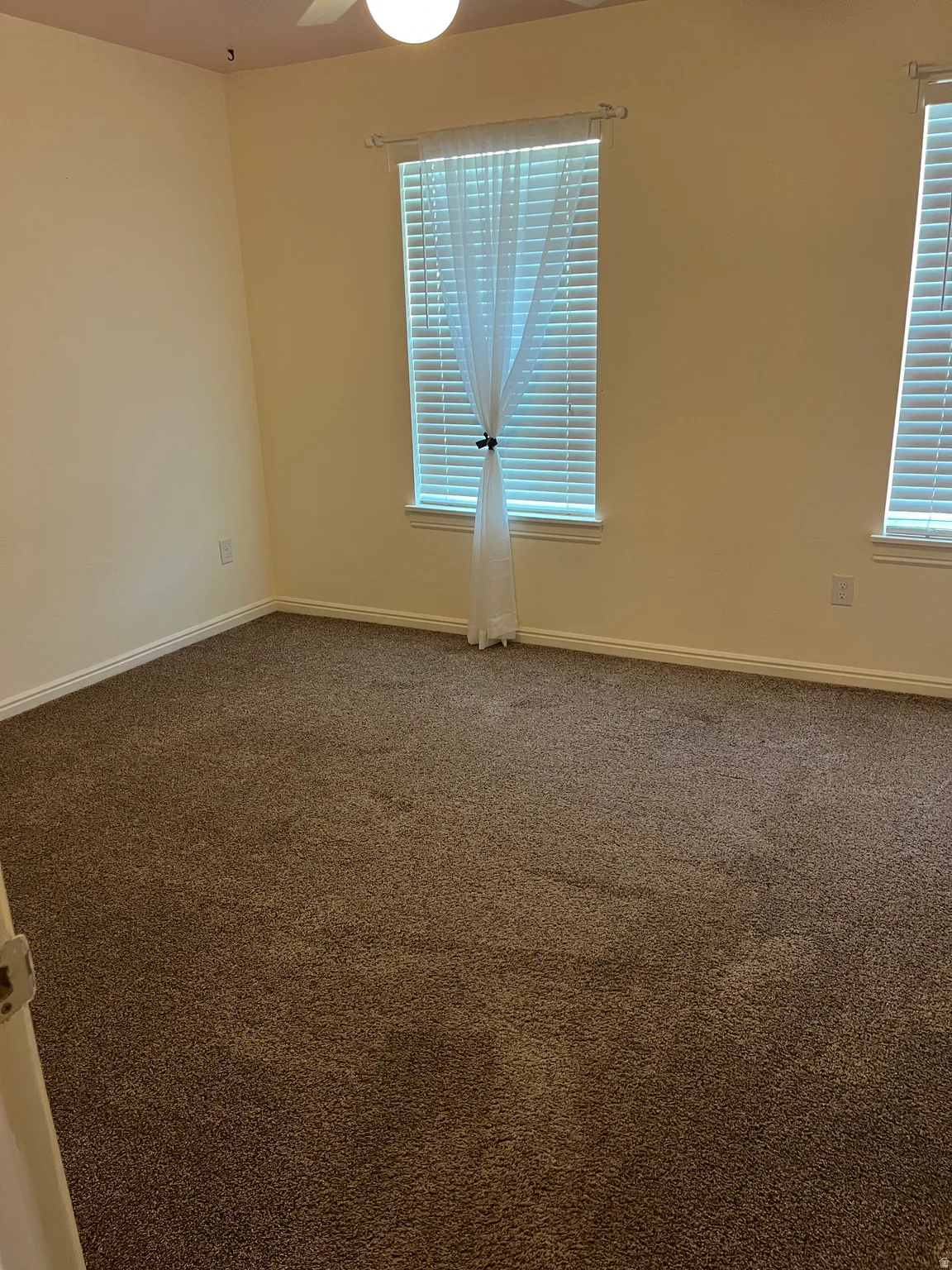 Spacious room featuring neutral-toned walls, brown carpeting, and a ceiling fan with integrated lighting