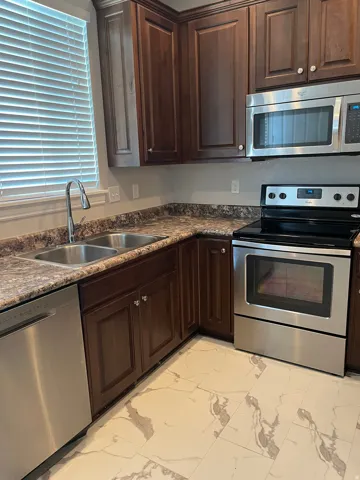 Kitchen featuring dark wood cabinetry, stainless steel appliances, a double basin sink, and patterned flooring
