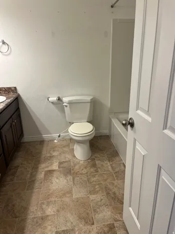 Bathroom featuring a white toilet, tile-patterned flooring, a dark wood-finish vanity with a countertop, and a white paneled door