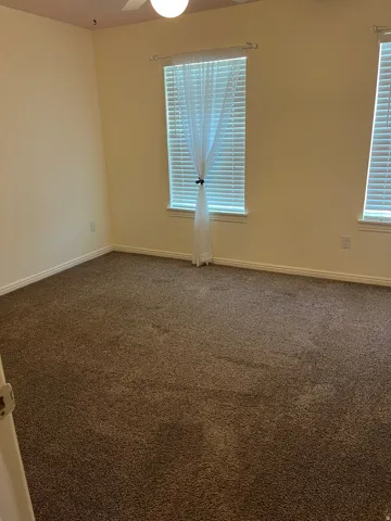 Spacious room featuring neutral-toned walls, brown carpeting, and a ceiling fan with integrated lighting