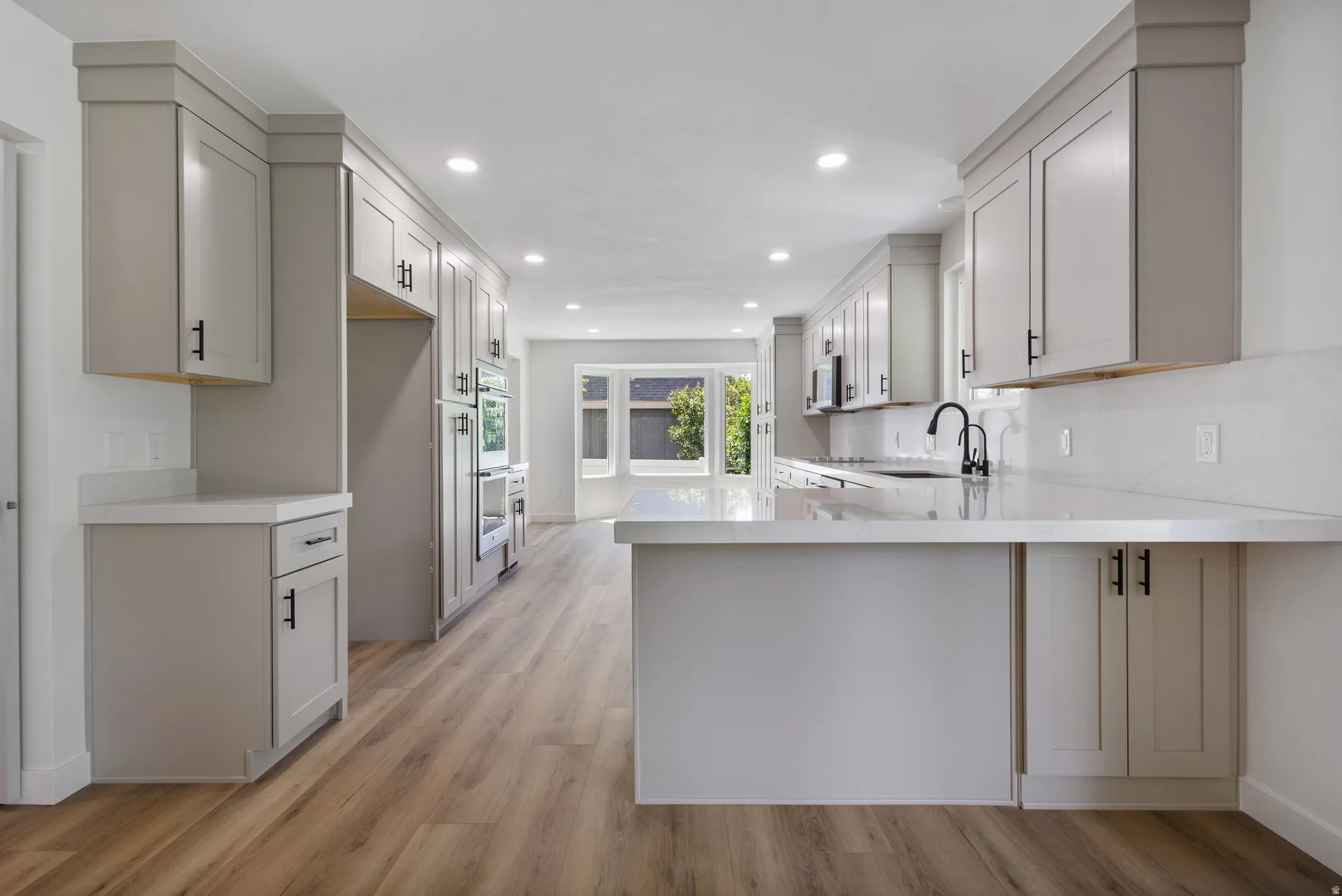 Kitchen featuring light gray cabinetry, built-in double ovens, wood-finish flooring, white countertops, and a black gooseneck faucet