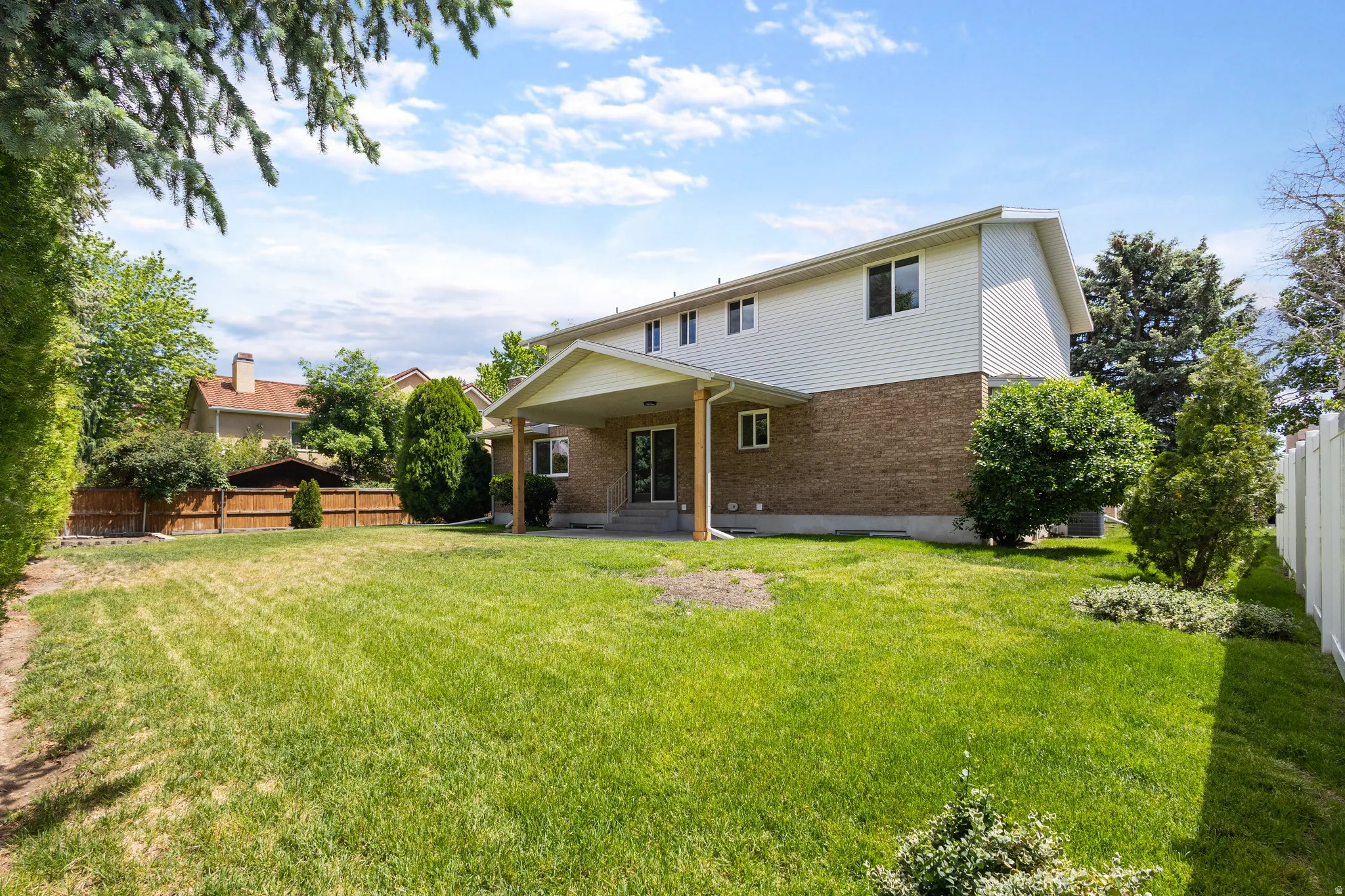 Expansive backyard featuring a covered patio, brick and siding exterior, large windows, mature perimeter trees, and a privacy fence