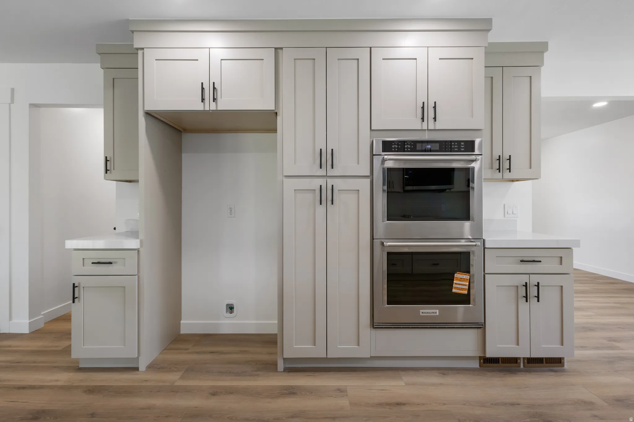 Light gray shaker-style cabinetry with matte black hardware, white countertops, and stainless steel double ovens