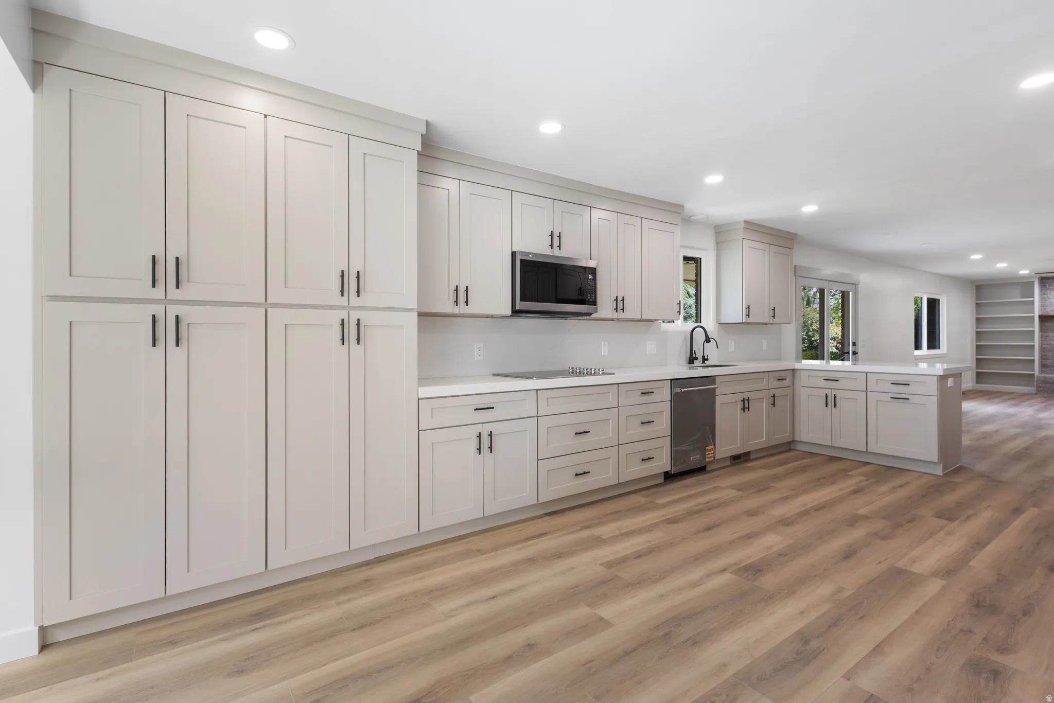Contemporary kitchen featuring extensive light cabinetry with matte black hardware, white countertops, stainless steel appliances, and recessed lighting