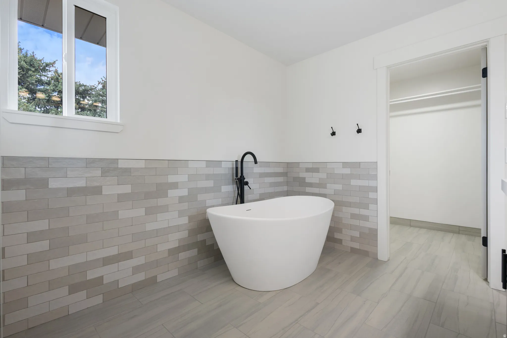 Freestanding soaking tub with matte black floor-mounted faucet, complemented by a light-toned tile accent wall