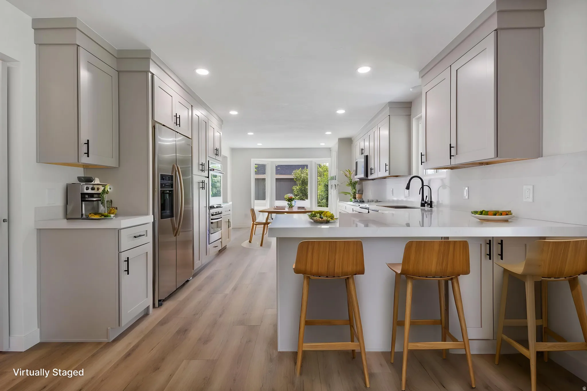 Contemporary kitchen featuring extensive light gray cabinetry, stainless steel appliances, wood-finish flooring, recessed lighting, and a kitchen island with a light-toned countertop