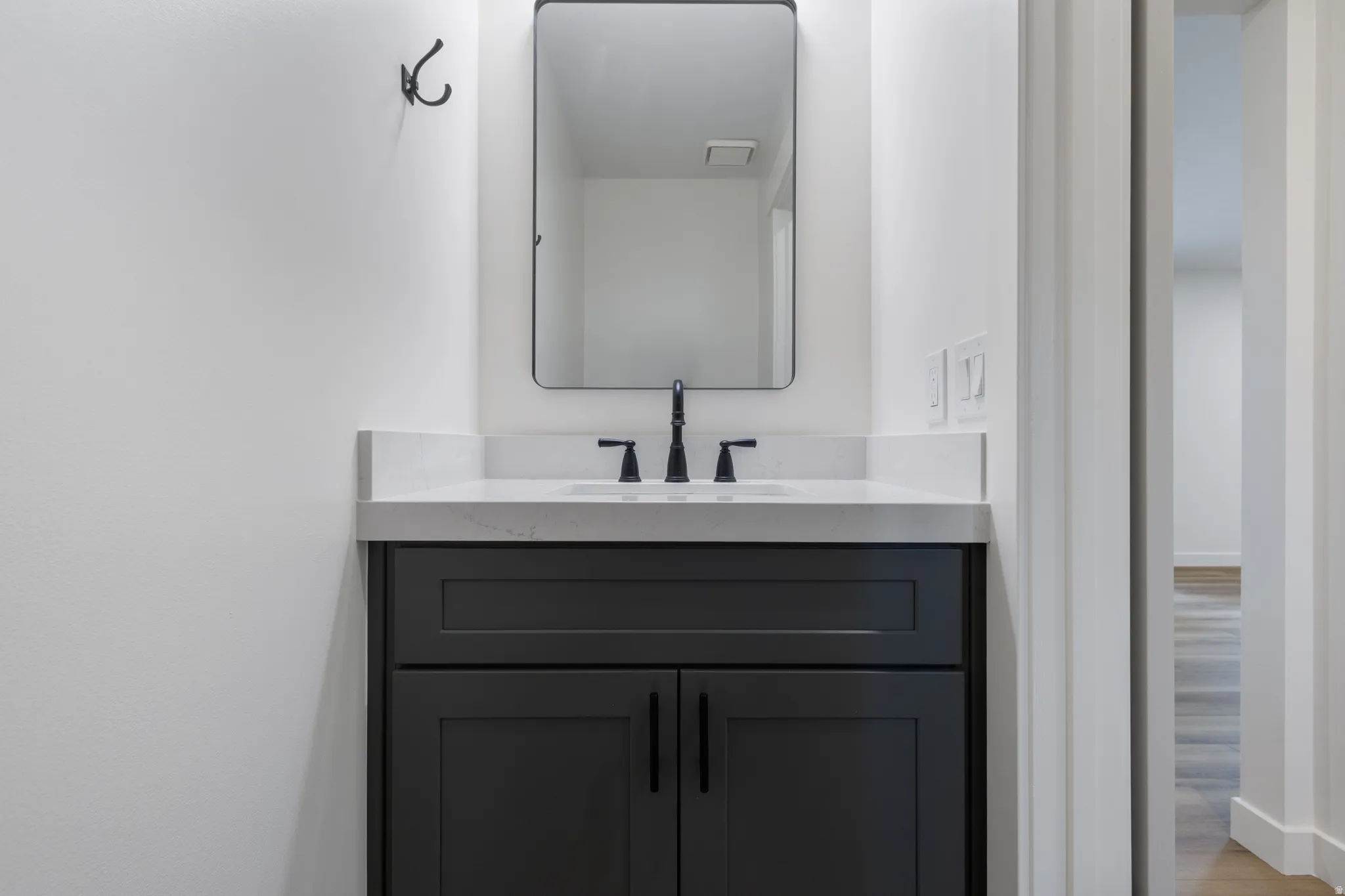 Contemporary vanity featuring a dark gray cabinet, a white countertop, and a rectangular undermount sink with a matte black faucet