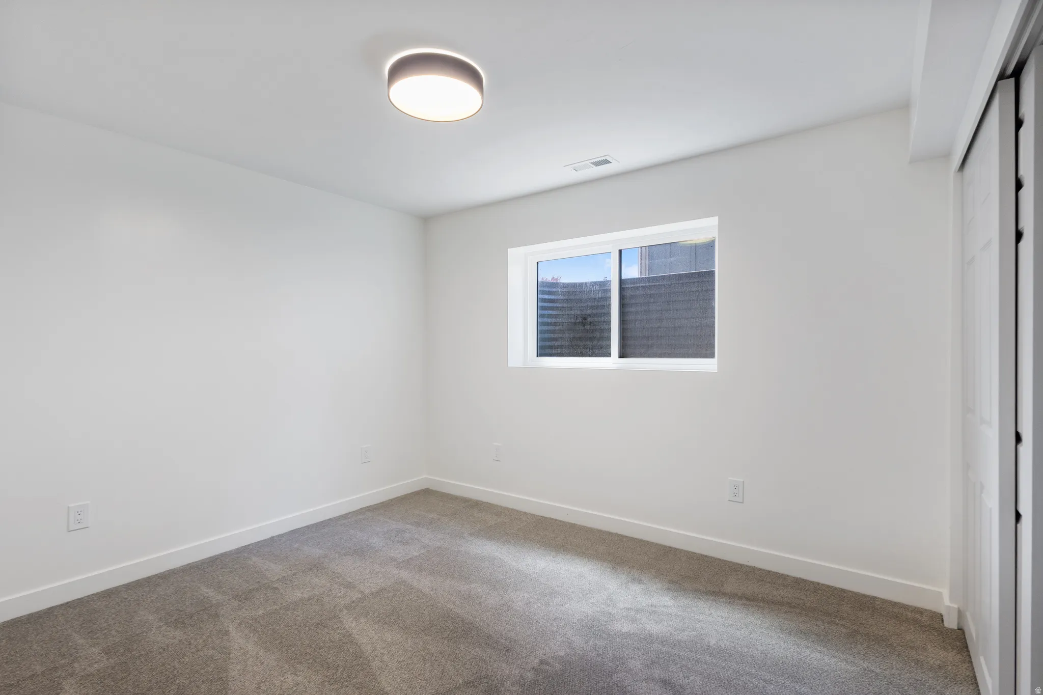 Room featuring neutral gray carpet flooring, white walls, and a modern flush-mount ceiling light fixture