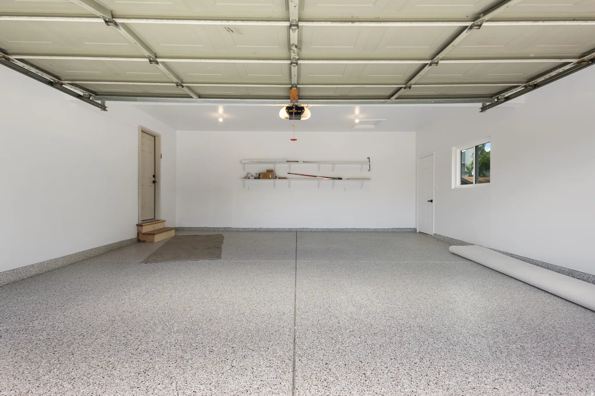Spacious garage featuring a durable epoxy floor coating, crisp white walls, recessed lighting, a built-in shelving unit, and a window providing natural illumination