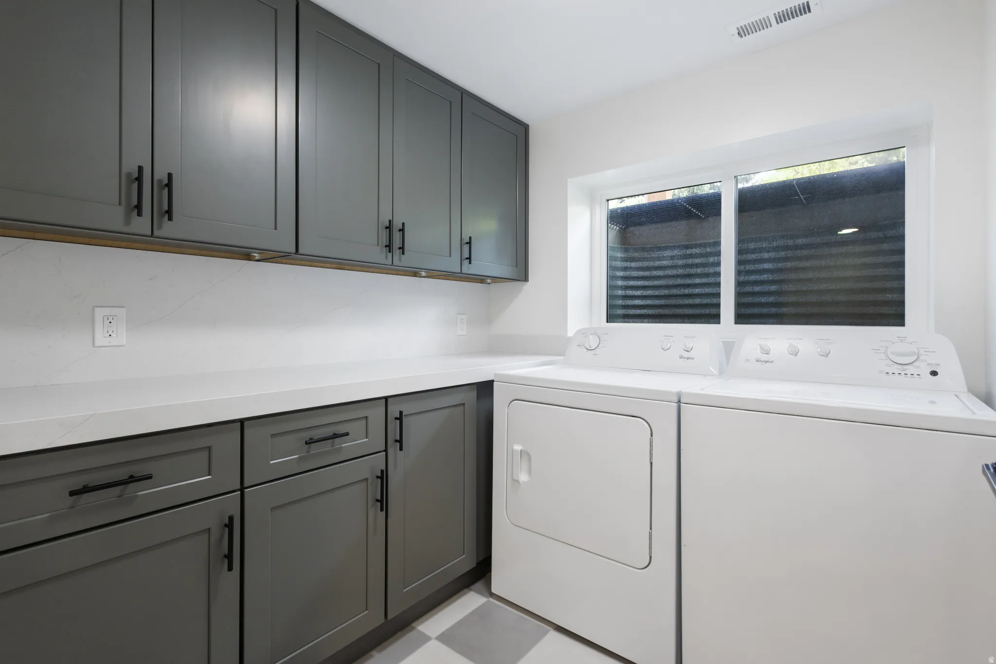 Laundry room featuring a window, gray shaker cabinetry, white countertops, and a checkered floor pattern