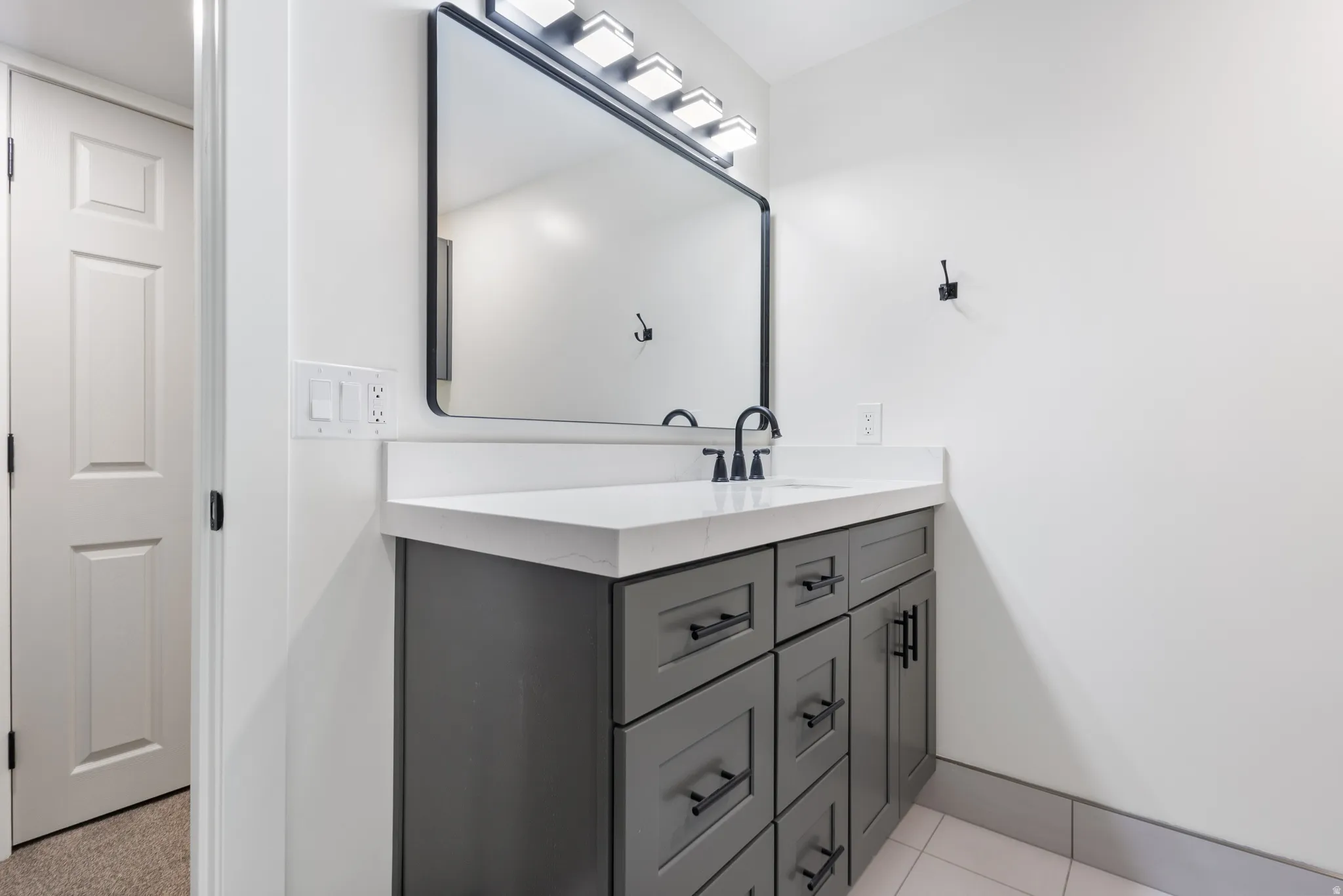 Bathroom vanity featuring a rectangular framed mirror, a four-light fixture, a solid surface countertop, a single basin sink, and a matte black faucet