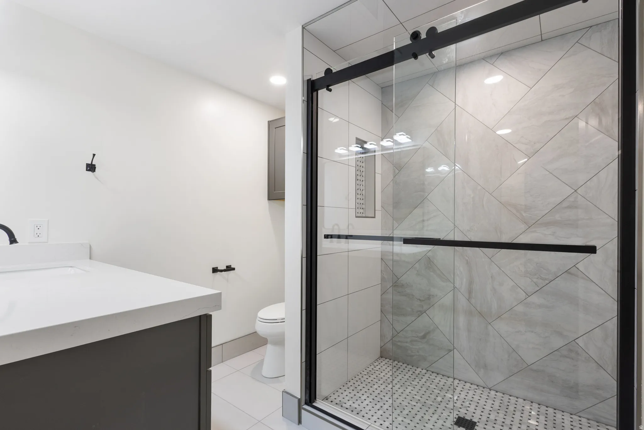 Contemporary bathroom featuring a spacious glass-enclosed shower with black-framed sliding door and geometric tile surround