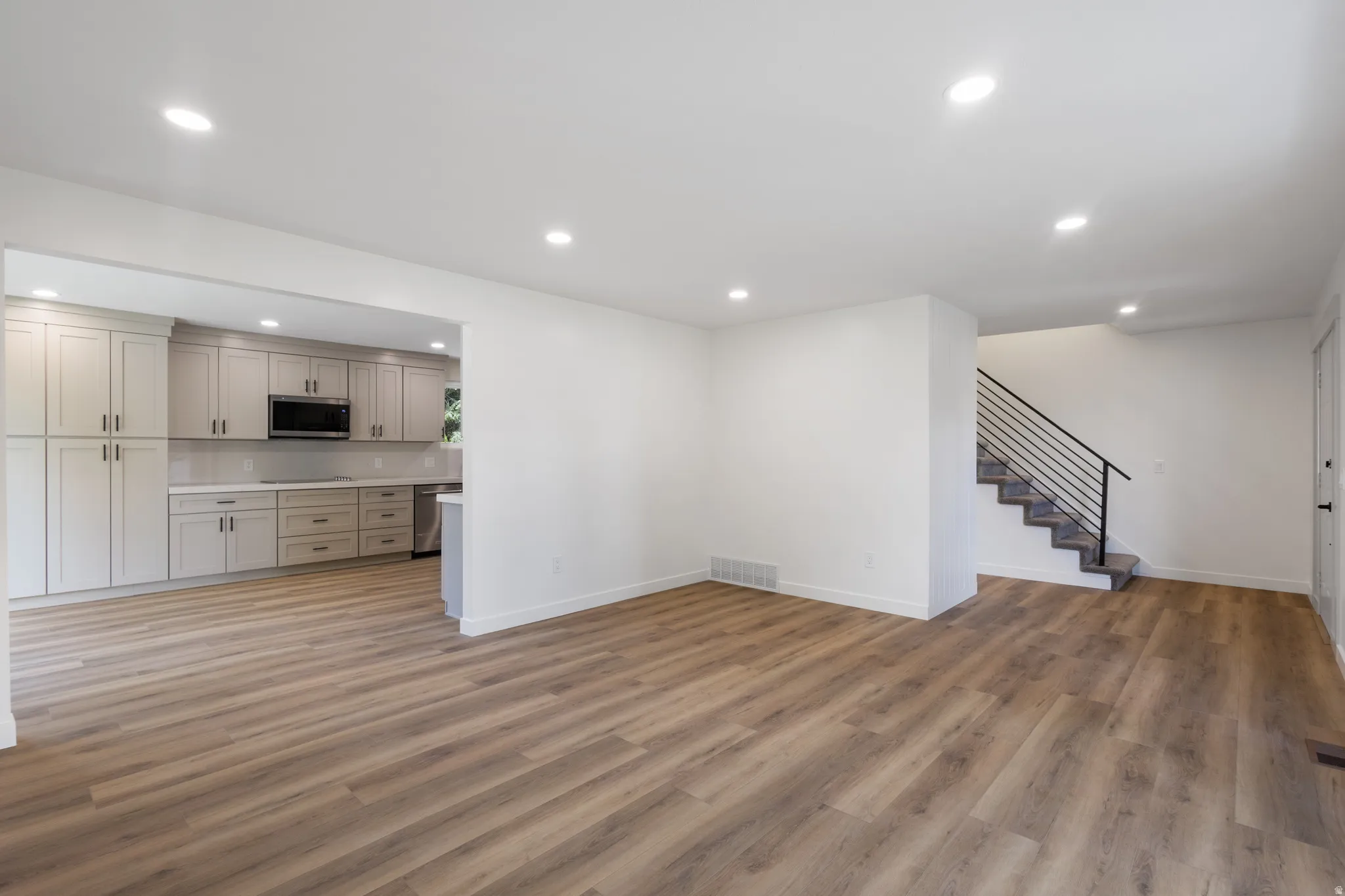 Open-concept living area with wood-finish flooring, recessed lighting, and a modern kitchen featuring grey cabinetry, stainless steel appliances, and a tiled backsplash