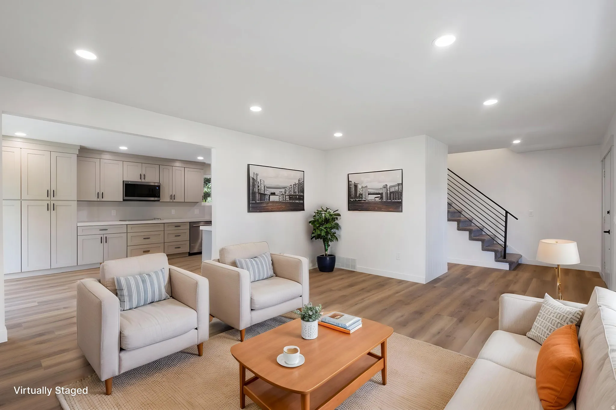 Open-concept living space featuring wood-finish flooring, recessed lighting, and a modern staircase with a black metal railing