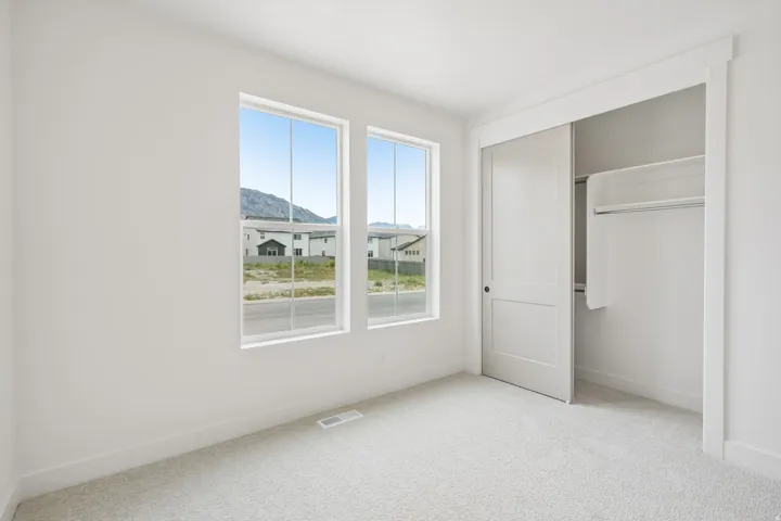 Room with two large windows, light gray carpet, white baseboards, and a closet featuring a white sliding door and built-in shelving