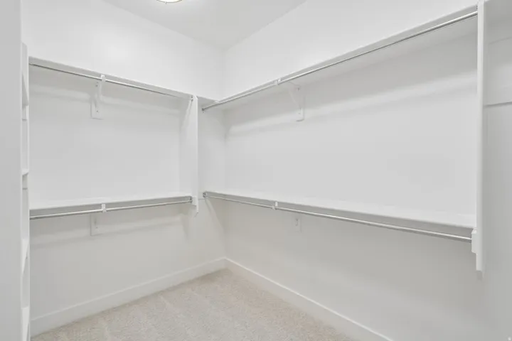 Walk-in closet featuring white walls, white shelving, metal hanging rods, and light-toned carpeting