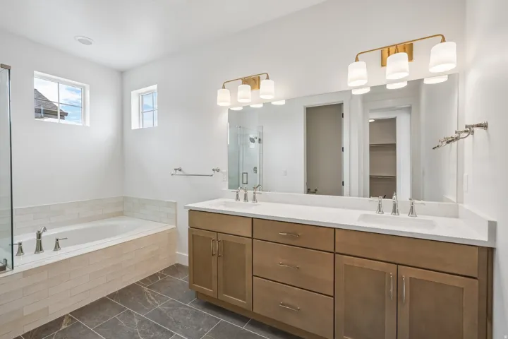 Bathroom featuring a built-in soaking tub with subway tile surround, a spacious double vanity with integrated sinks and a large mirror, and matte finish floor tiling
