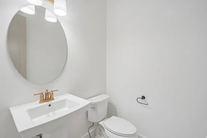 Bathroom featuring a pedestal sink, gold-tone faucet, round mirror, and a two-bulb vanity light