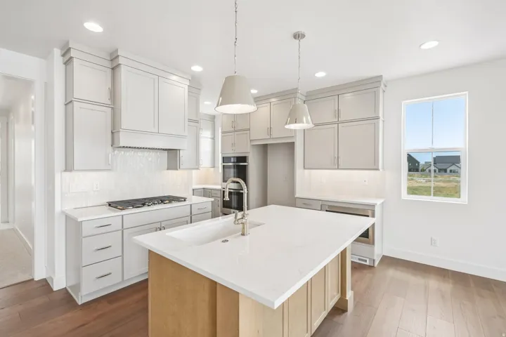 Spacious kitchen featuring an expansive central island with an integrated sink, light-toned cabinetry, stainless steel appliances, a tile backsplash, and wood-finish flooring