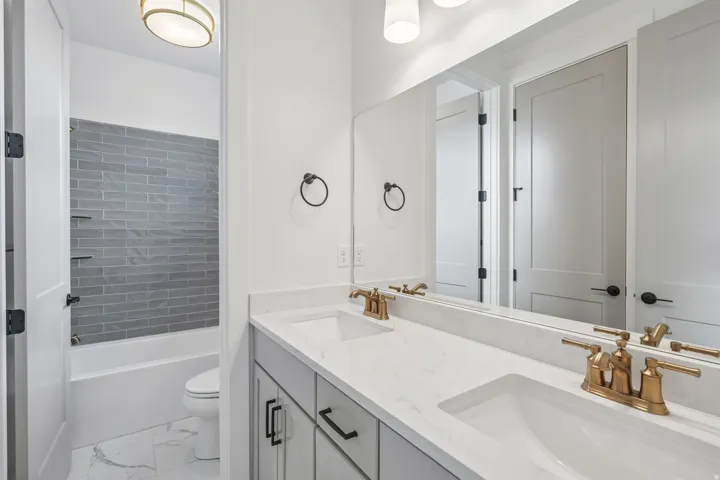 Bathroom with dual vanity featuring white undermount sinks, bronze-finish faucets, and a full-width mirror