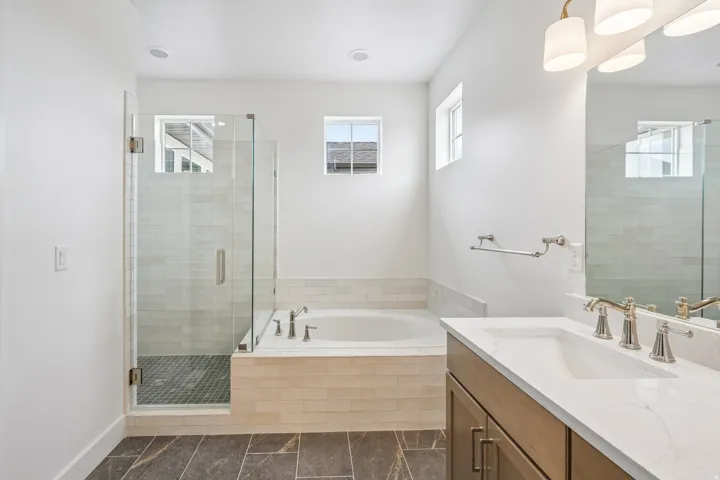Full bathroom featuring a glass-enclosed shower, built-in soaking tub with tile surround, wood-finish vanity with dual sinks, and a large mirror