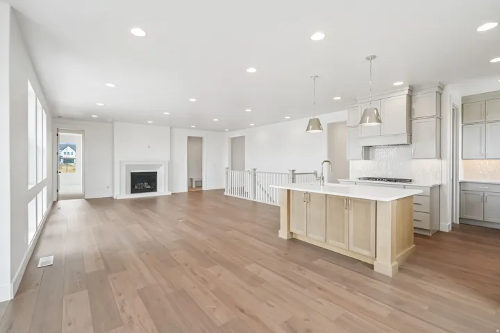 Open-concept interior featuring wood-finish flooring, recessed lighting, and a white stone-clad fireplace