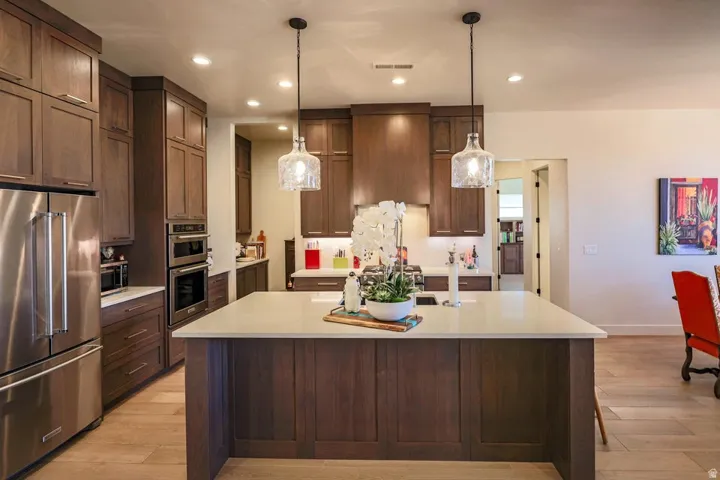Kitchen featuring stainless steel appliances, dark wood-finish cabinetry, a central island with a light-toned countertop, and two pendant light fixtures