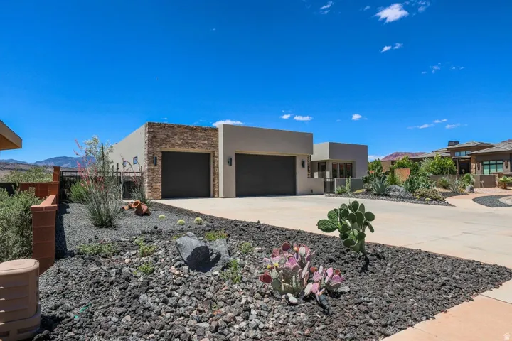Stucco exterior with stone accents, two garage doors, concrete driveway, and xeriscaped landscaping
