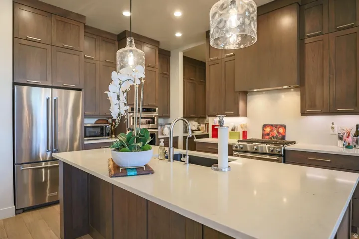 Gourmet kitchen featuring stainless steel appliances, a center island with a light-toned countertop, dark wood-finish cabinetry, and pendant lighting