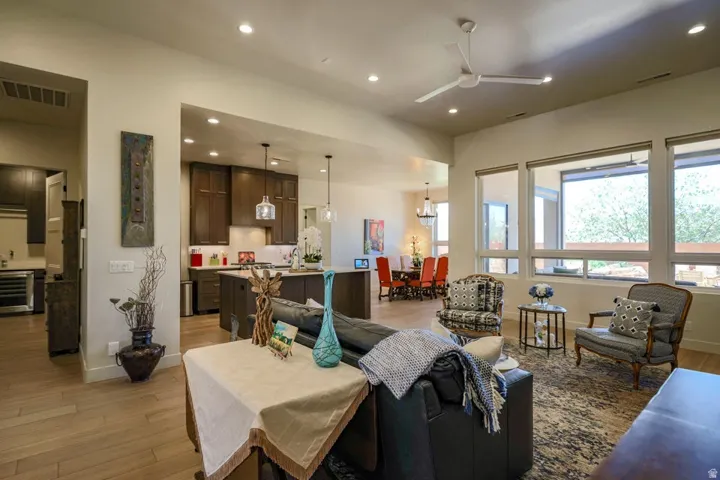 Recessed lighting throughout, wood-finish flooring, ceiling fan, expansive windows, and a kitchen with dark wood cabinetry and pendant lighting