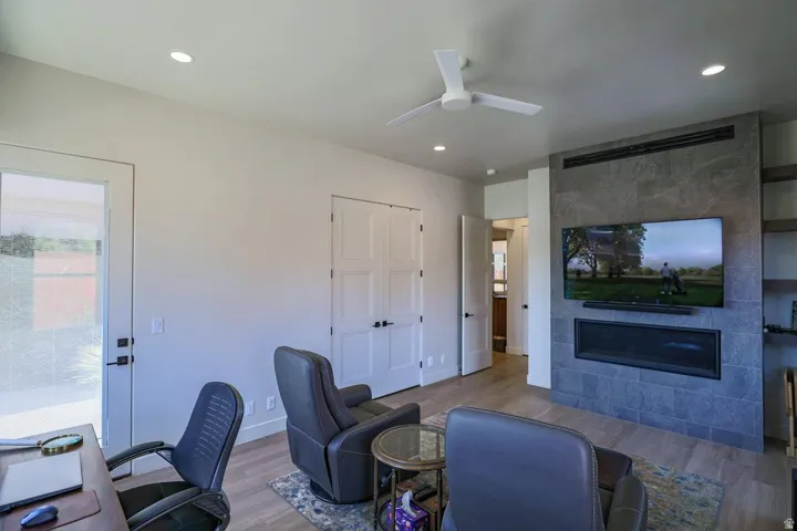 Built-in linear fireplace, recessed lighting, wood-finish flooring, ceiling fan, and a glass-paneled exterior door