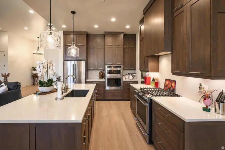 Full kitchen with wood-finish cabinetry, stainless steel appliances, light-toned countertops, and wood-finish flooring