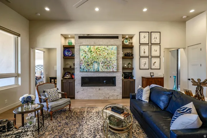 Living area featuring a floor-to-ceiling stone-clad fireplace, integrated built-in shelving, wood-finish flooring, and recessed lighting